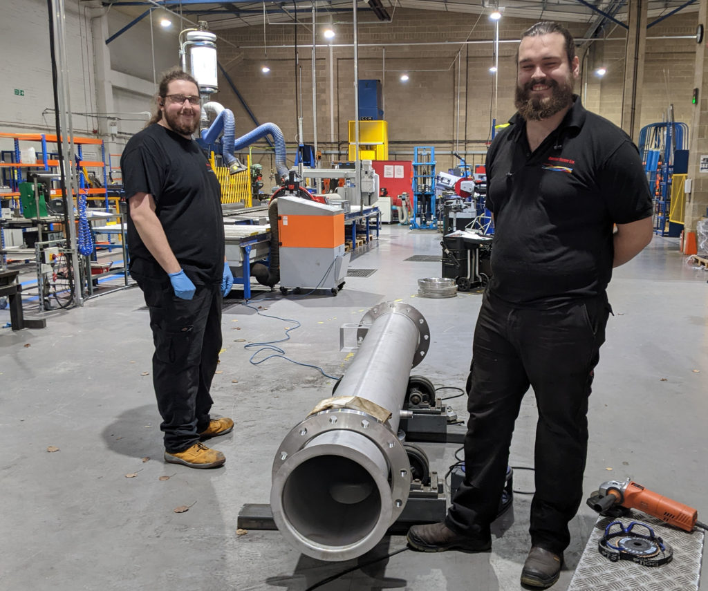 Two Amazon Filters employees stand either side of a manufactured metal tube in the firm's dedicated production hub